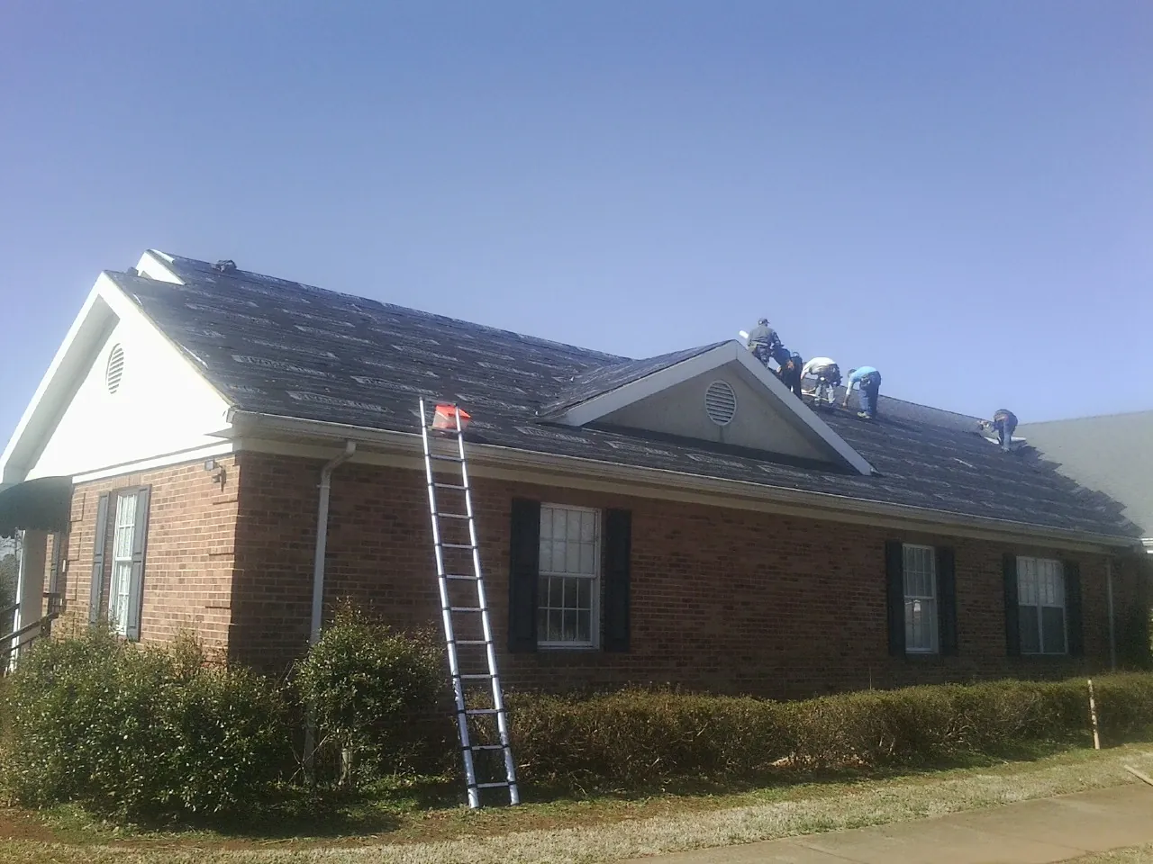 Crew tearing shingles off a brick ranch roof with a ladder set — Emergency Roof Repair work by our crew in Round Mountain