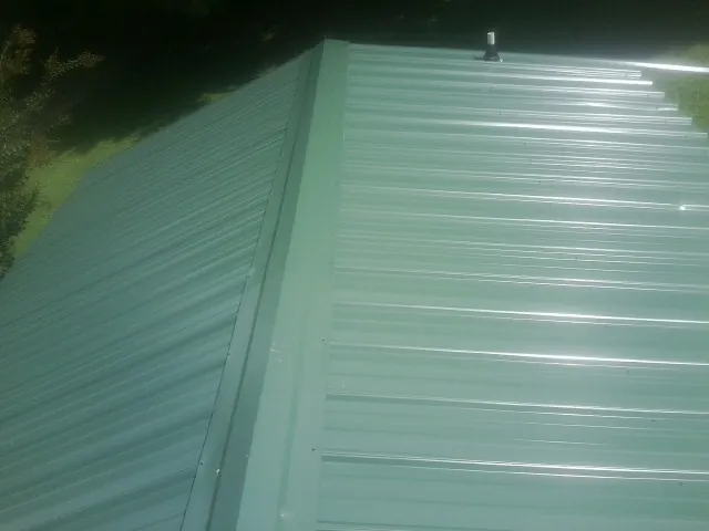 New green metal panels meeting at the ridge of a roof — Flat Roof Repair work by our crew in Round Mountain